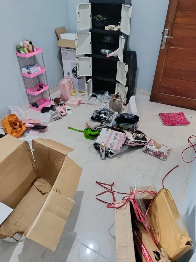 Sebelum: kamar penuh kardus terbuka, plastik, pakaian, dan barang pindahan berserakan di lantai